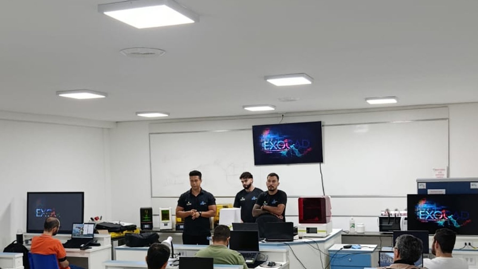 Três instrutores trabalhando em bancadas da sala técnica do Instituto