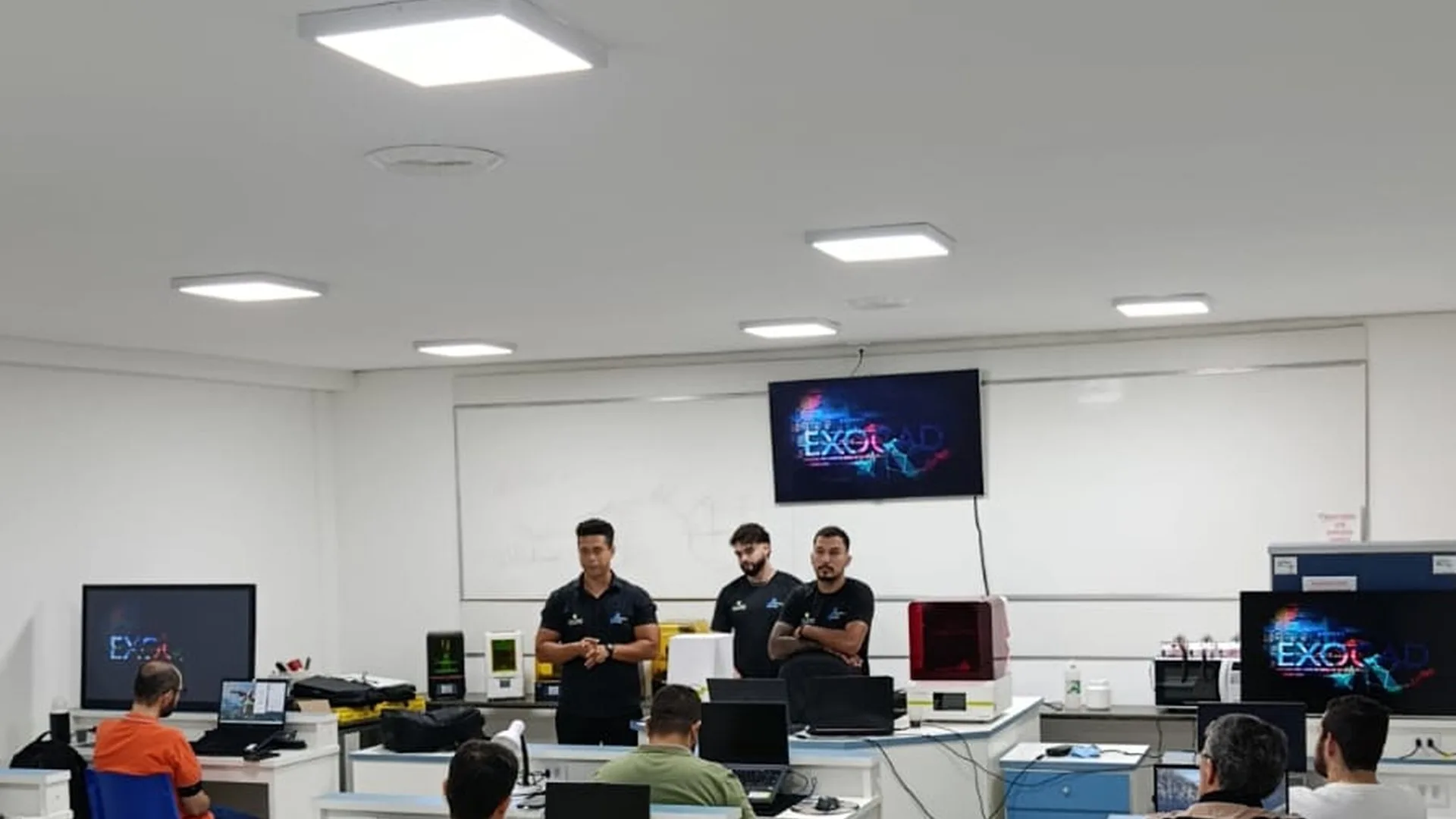 Três instrutores trabalhando em bancadas da sala técnica do Instituto