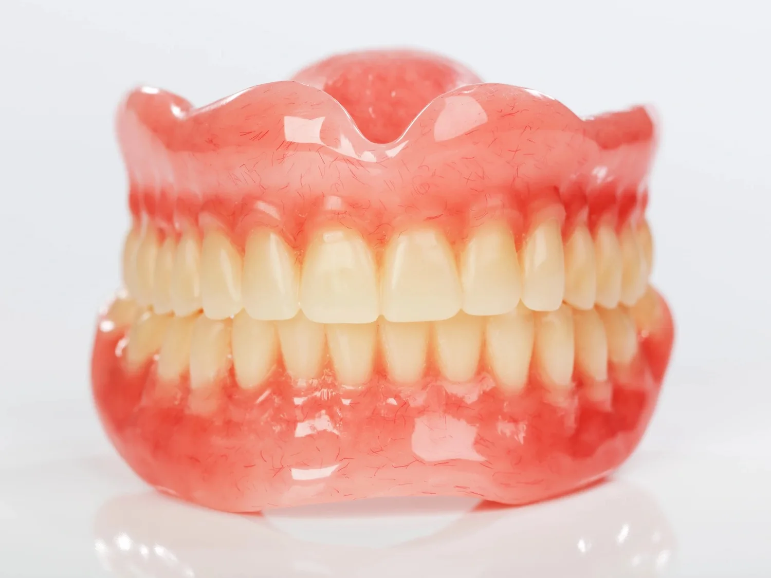 Prótese total em base rosa com dentes caracterizados, sobre fundo neutro